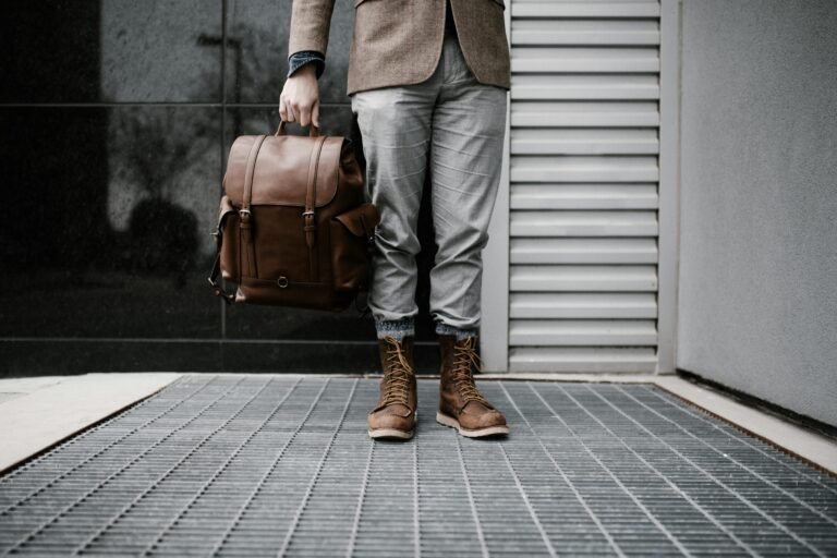 A man in stylish attire holding a leather backpack outdoors.