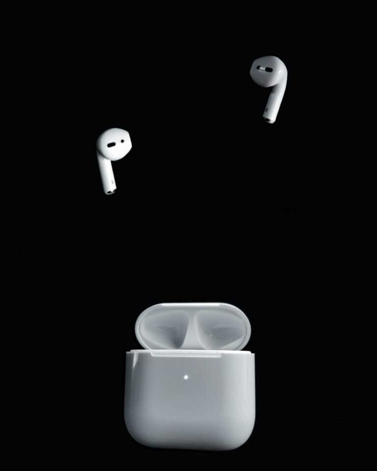Minimalist image of wireless earbuds and case suspended against a black background.